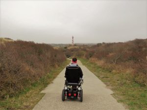 Wheelymum fährt mit dem Elektro-Rollstuhl hinter dem Deich